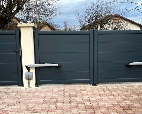 Portail battant gris anthracite motorisé - Design moderne Portail battant gris anthracite motorisé avec portillon assorti sur une allée en pavés.