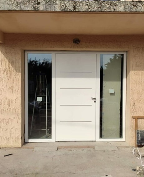 Porte d'entrée blanche moderne avec vitrage latéral Porte d'entrée blanche moderne à lignes horizontales et doubles vitrages latéraux dans une façade beige texturée.