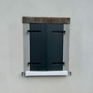 Volets Gris Anthracite et Linteau Bois pour Façade Fenêtre avec volets battants gris anthracite, encadrement en pierre, linteau bois et appui blanc sur mur crépi clair.