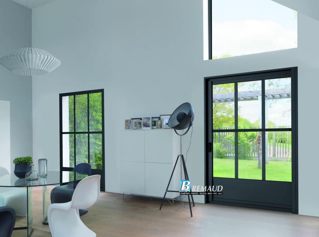Baie Coulissante Noire et Menuiserie Alu Brémaud Baie coulissante noire Brémaud dans un salon moderne lumineux avec fenêtres style atelier et mobilier design.