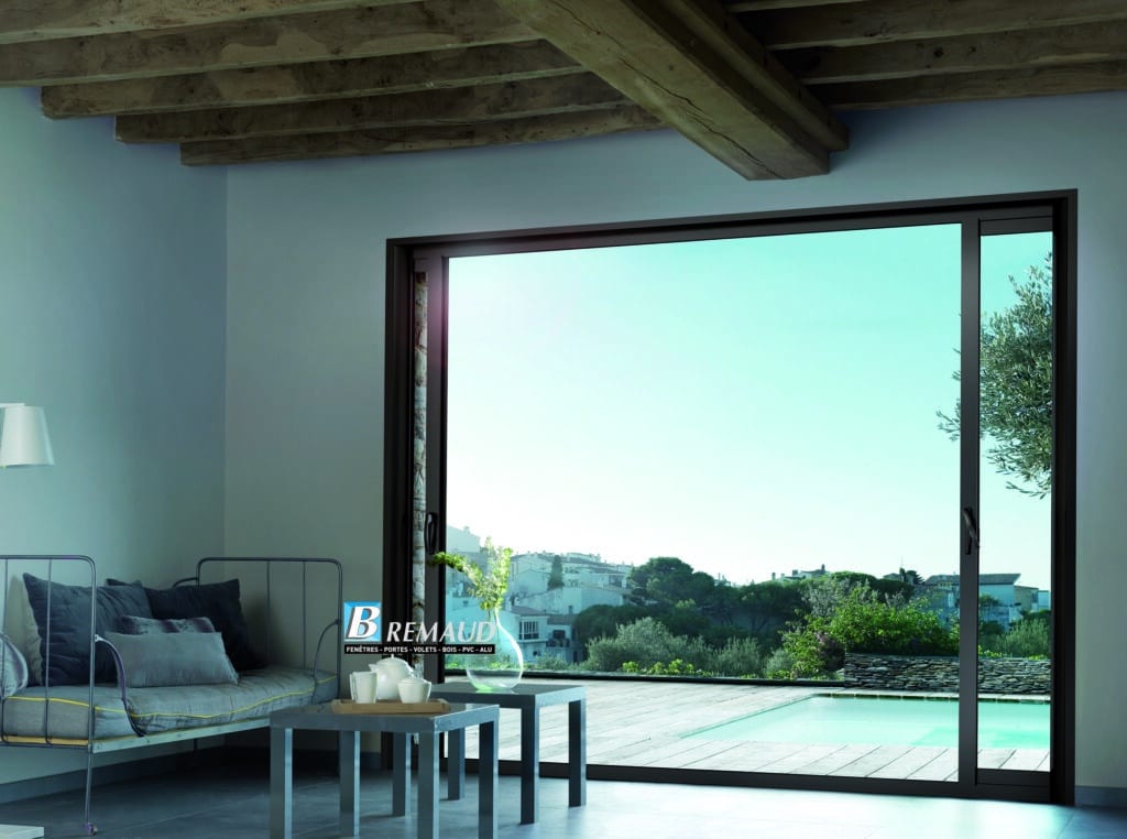 Baie Vitrée Coulissante Alu Remaud avec Vue sur Piscine Baie vitrée coulissante alu Remaud ouvrant sur terrasse avec piscine et vue panoramique sur un village côtier.