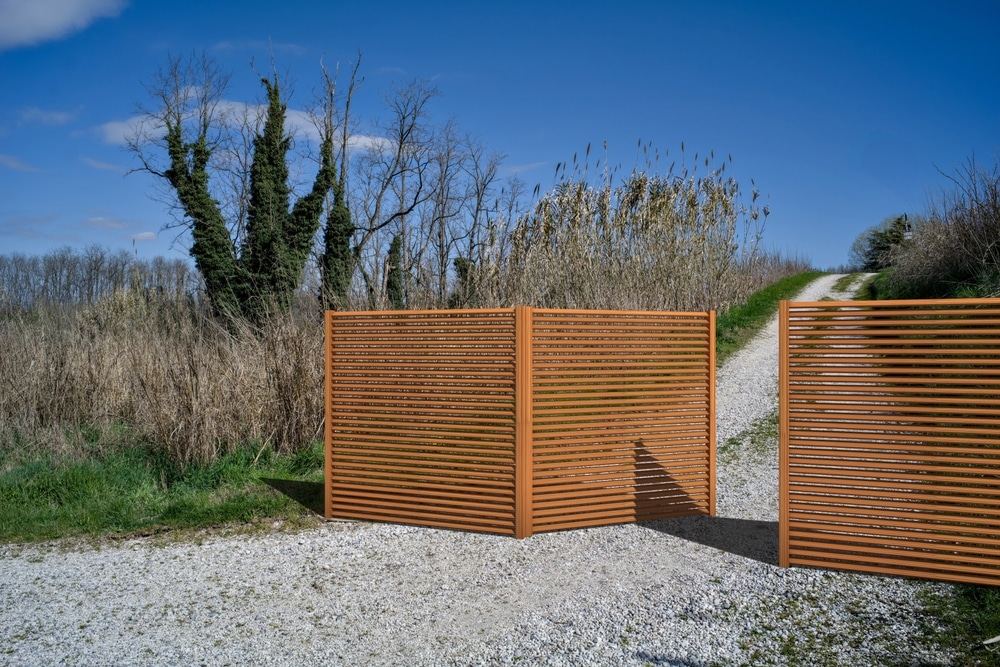 Clôture à lattes horizontales : pare-vue extérieur design Panneaux pare-vue à lattes bois sur chemin de gravier en pleine nature, aménagement extérieur moderne.