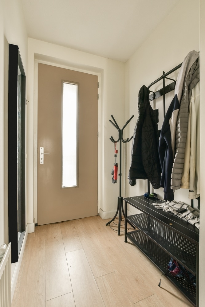 Aménagement d'entrée moderne avec rangement noir Entrée moderne avec porte beige, portemanteau noir, banc à chaussures et sol stratifié en bois clair.