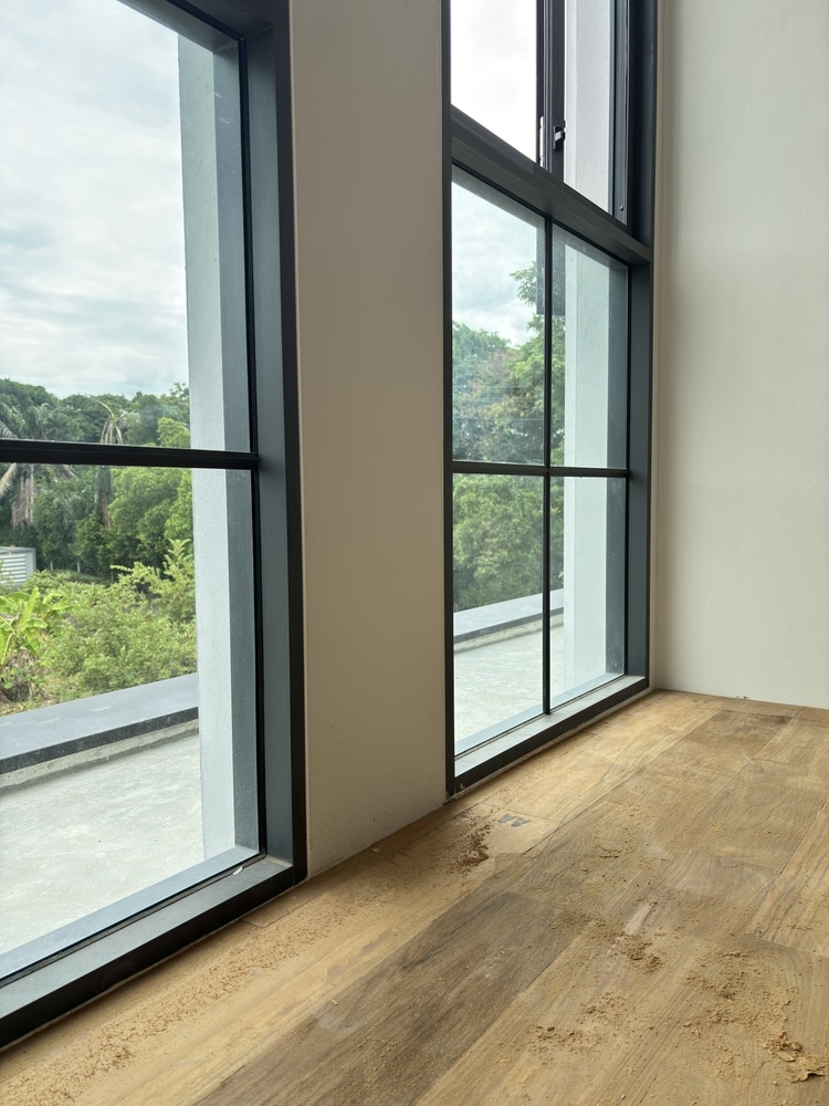 Fenêtres à Cadre Noir et Parquet en Bois en Travaux Grandes fenêtres à cadre noir avec vue sur un jardin et sciure sur un parquet en bois clair.