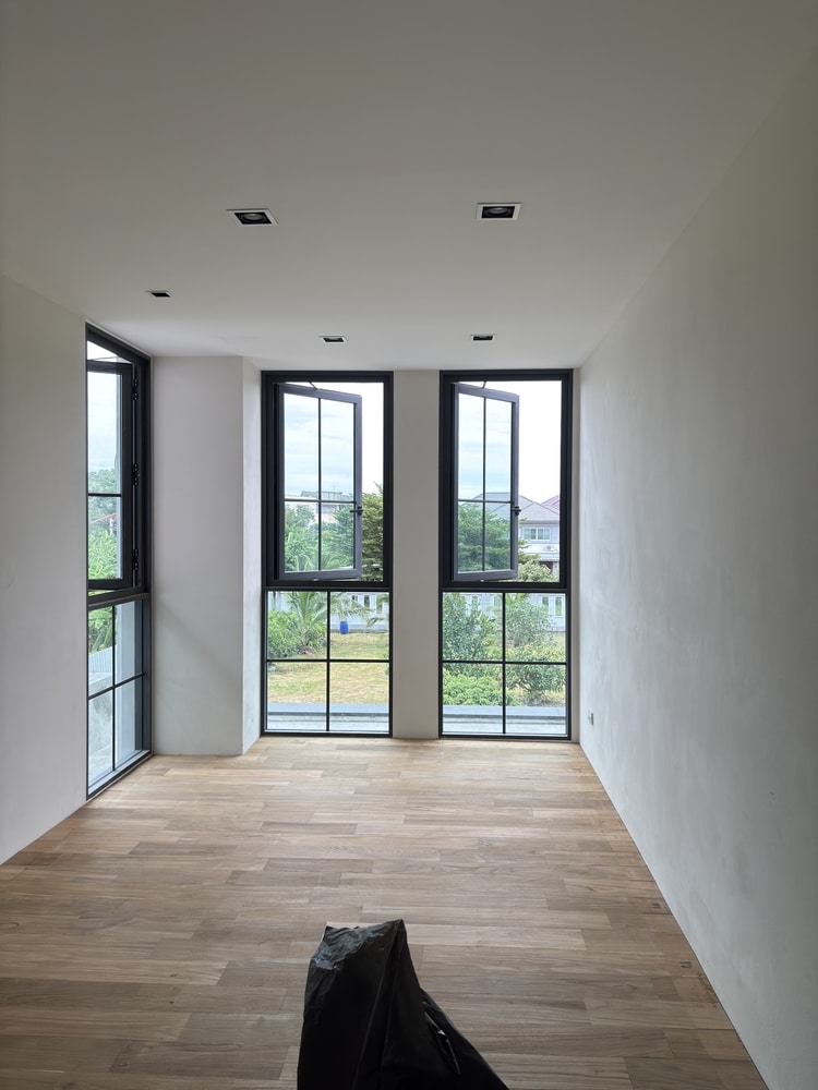 Design intérieur moderne : pièce vide avec parquet clair Intérieur moderne vide, parquet bois clair, fenêtres à cadre noir ouvertes sur jardin, spots encastrés au plafond.
