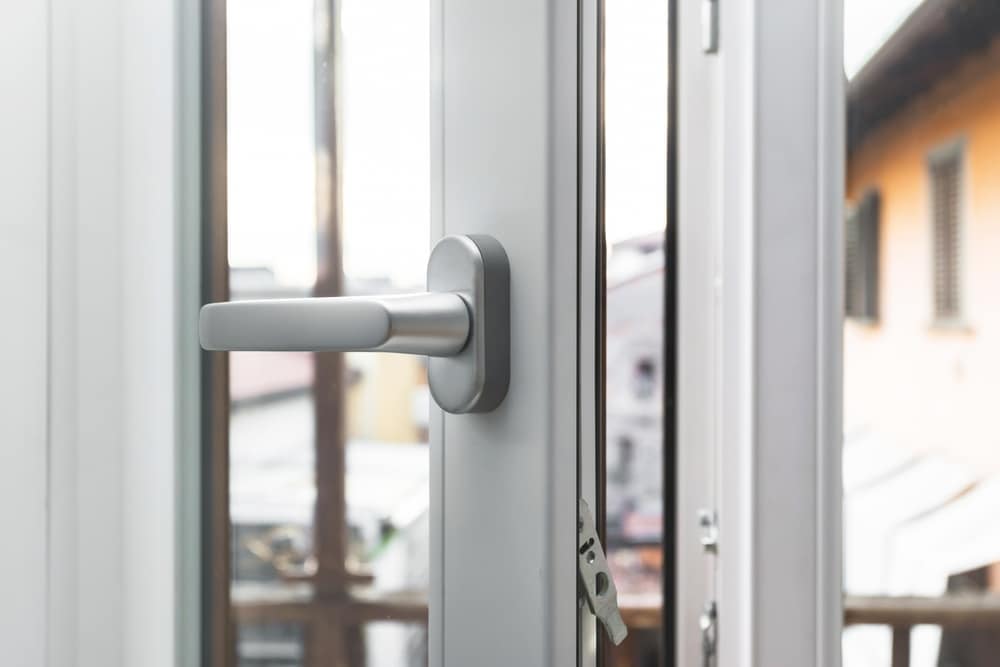 Poignée de fenêtre moderne en aluminium pour menuiserie Poignée de fenêtre moderne en aluminium gris sur un cadre blanc entrouvert avec vue floue sur l'extérieur.