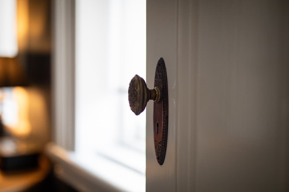 Poignée de porte ancienne vintage en bronze ciselé Poignée de porte ancienne en bronze ciselé sur une porte blanche, arrière-plan flou et lumineux.