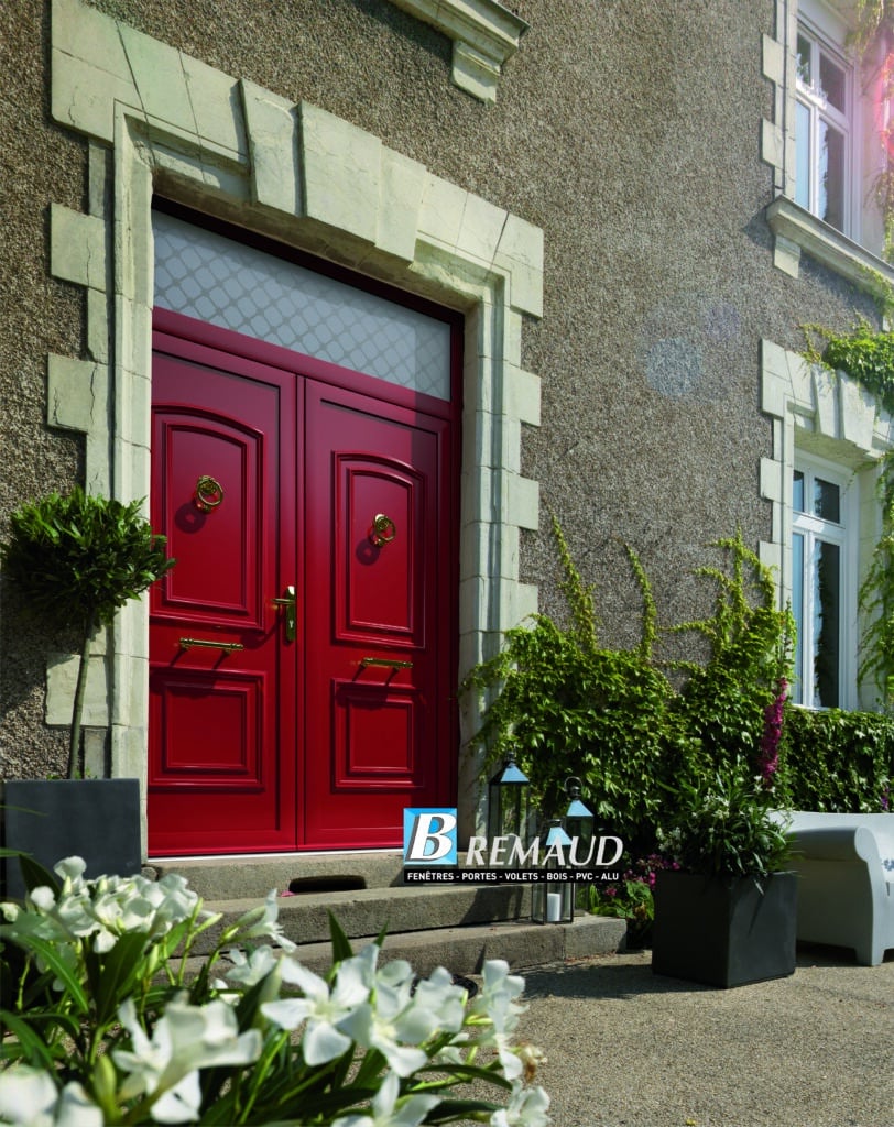 Porte d'Entrée Double Rouge Brémaud : Style Classique Double porte d'entrée rouge Brémaud avec heurtoirs dorés dans une façade en pierre, style classique élégant.