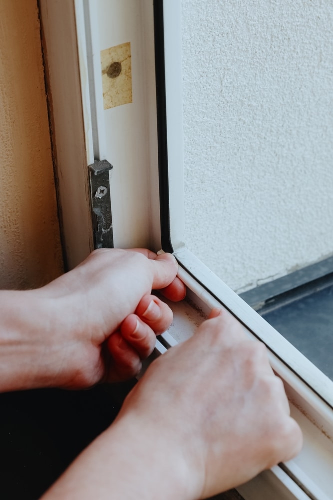 Pose joint étanchéité fenêtre pour isolation thermique Mains posant un joint d'étanchéité blanc sur un cadre de fenêtre pour une meilleure isolation thermique.