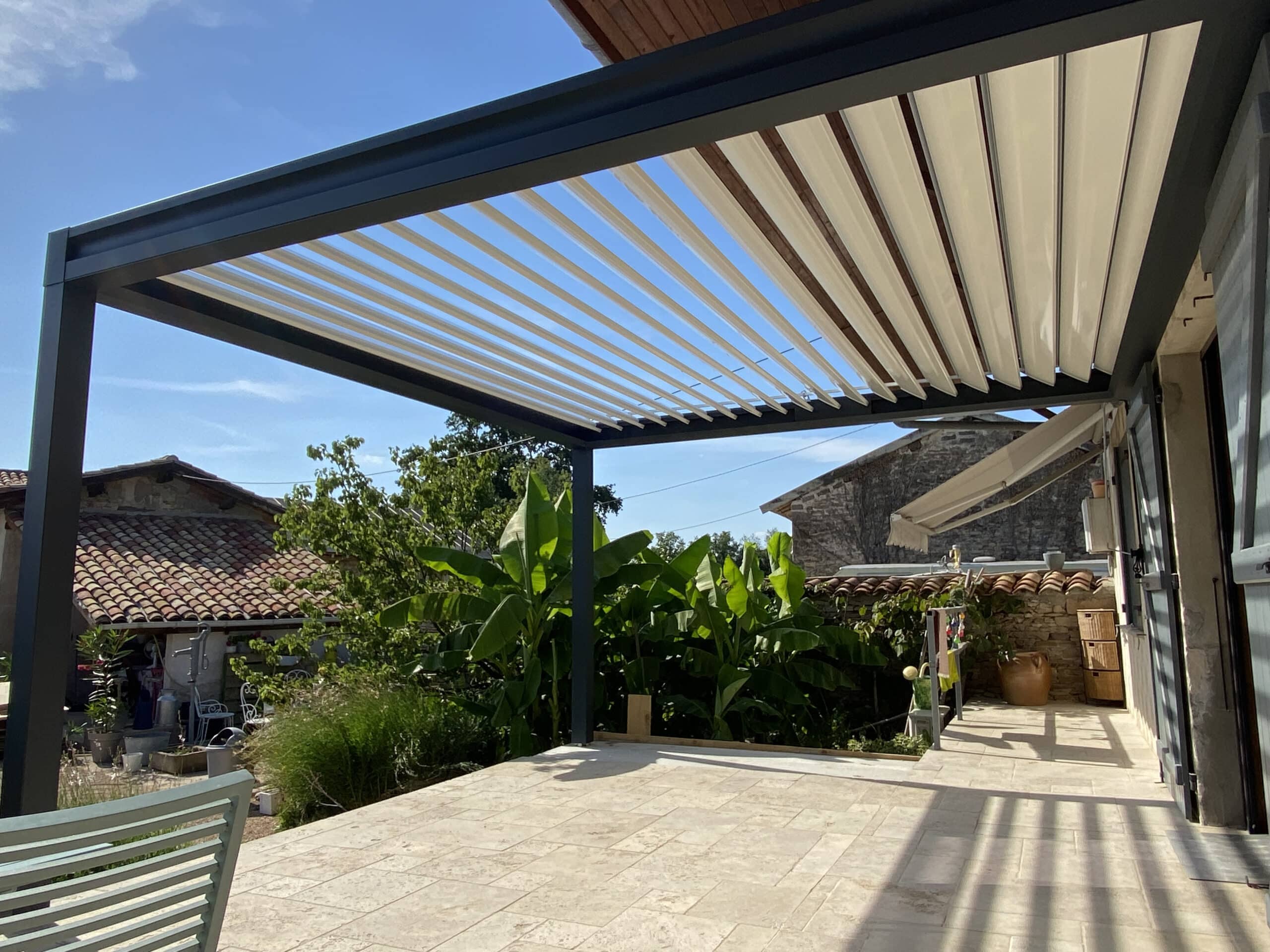 Pergola bioclimatique en aluminium gris sur une terrasse moderne en pierre entourée de bananiers.