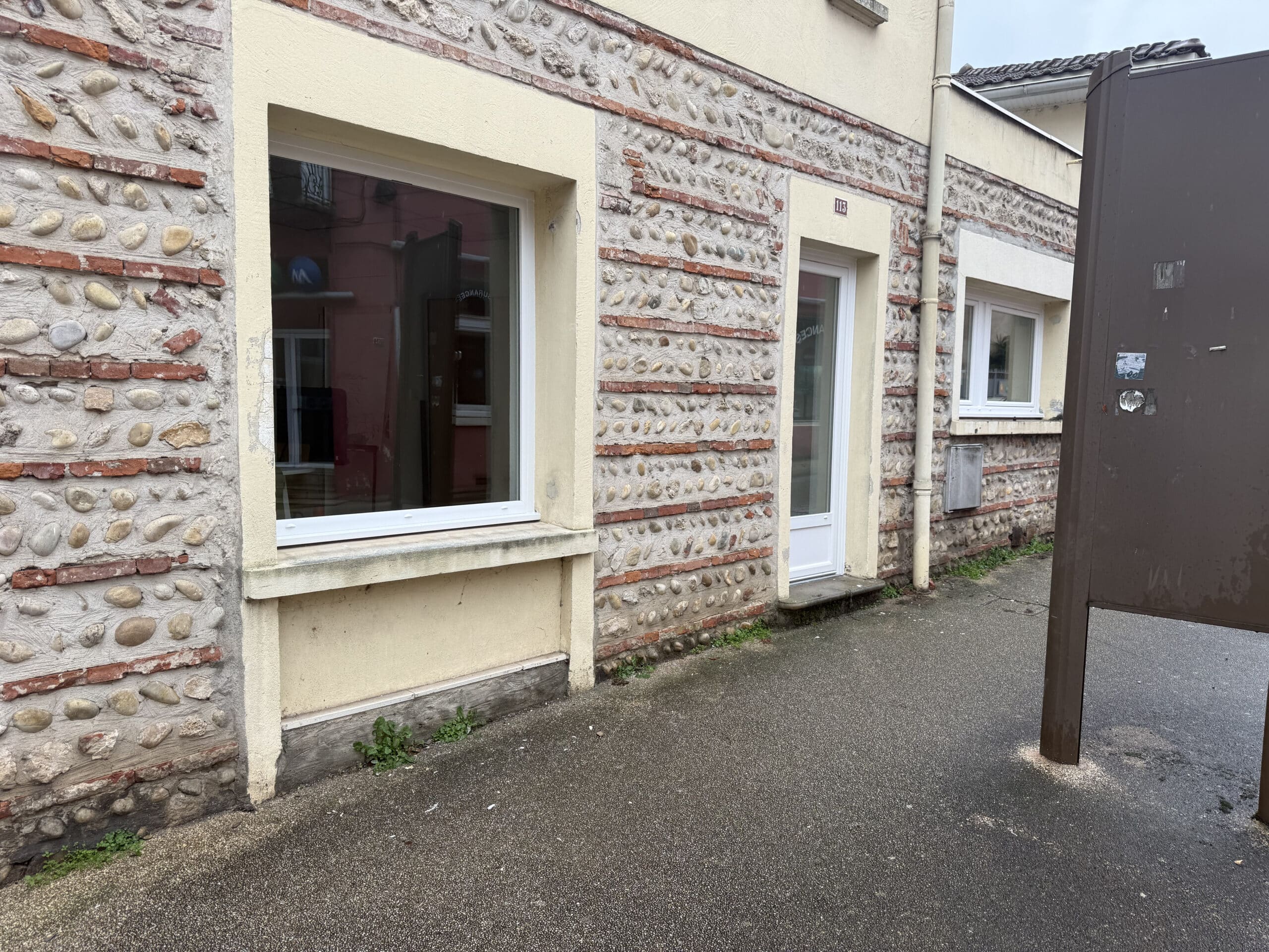 Façade en galets et briques avec fenêtre blanche et porte numéro 113.