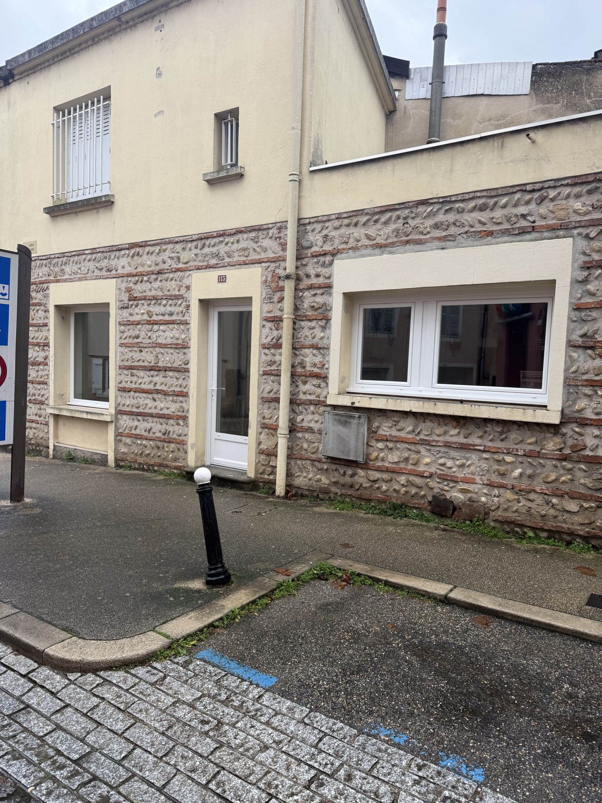 Maison n°113 en galets et briques avec menuiseries blanches et trottoir.