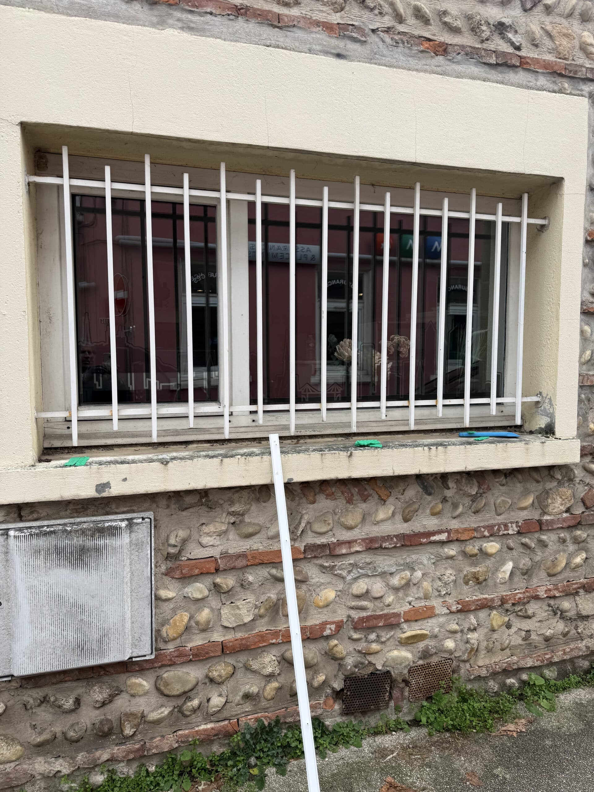 Fenêtre à barreaux blancs sur mur de pierre et brique avec baguette PVC.
