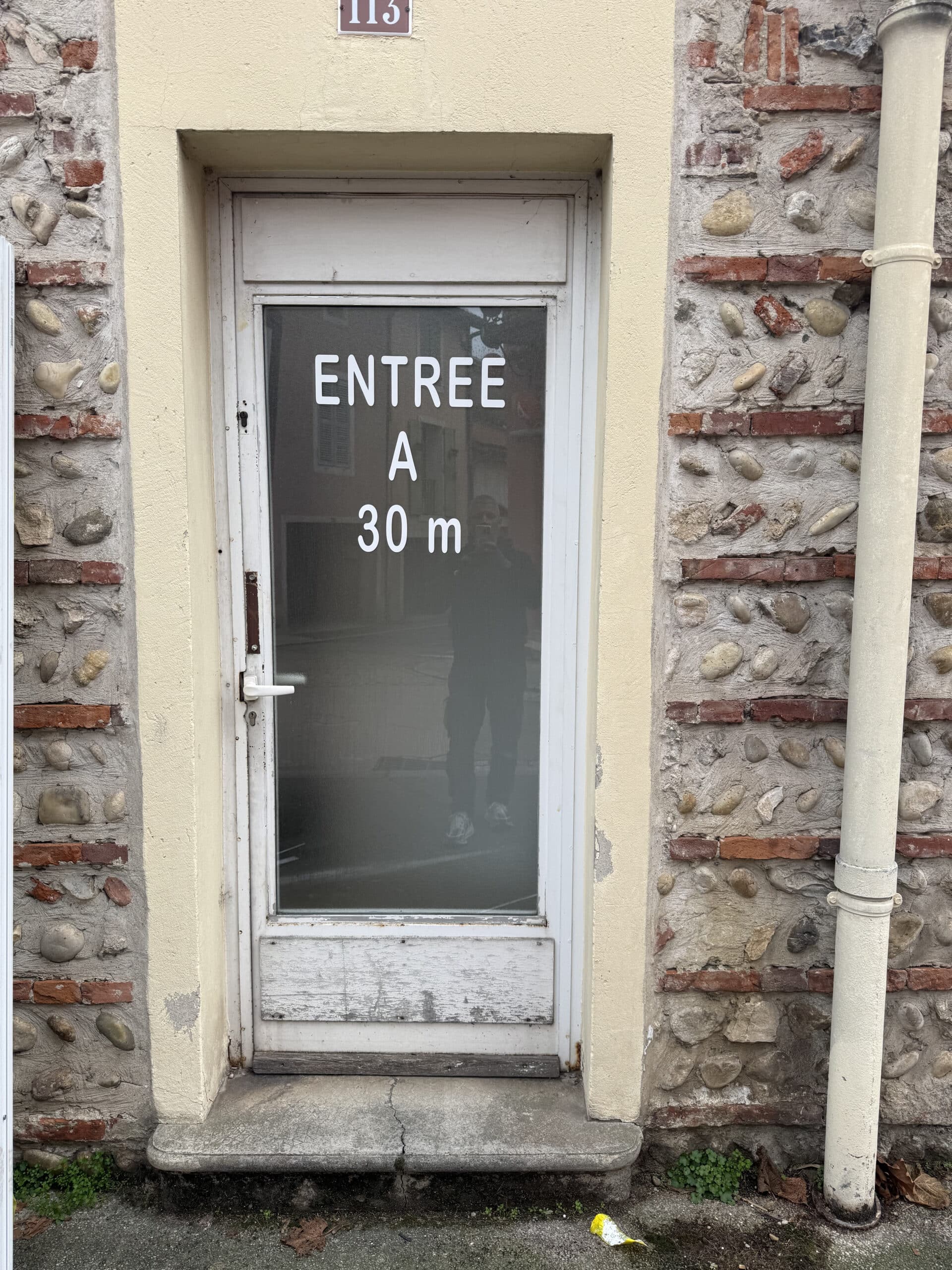 Porte vitrée n°113, mur pierre et brique, texte 'ENTREE A 30 m'. Signalétique entrée bâtiment ancien.